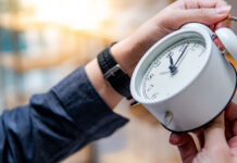 egy férfi kéz egy fehér klasszikus órát állít