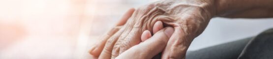 egy idős kezét fogja egy fiatal felnőtt
