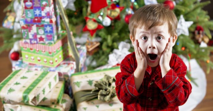 Big,Christmas,Surprise,/,The,Young,Lad,Is,Astonished,/ kisfiú meglepődve a karácsonyfa előtt. a fa alatt sok becsomagolt ajándék.
