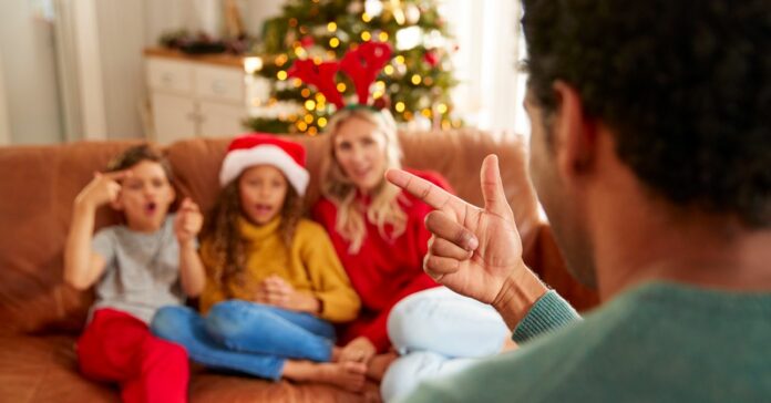 Family,Sitting,On,Sofa,Playing,Game,Of,Charades,At,Christmas Karácsonyi játékok gyerekeknek és felnőtteknek
