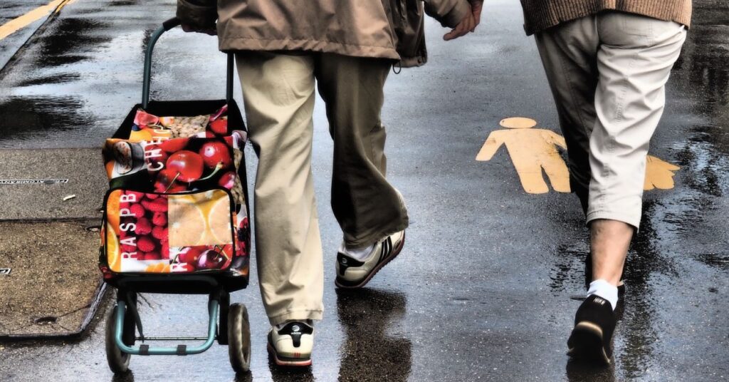 nyugdíjas férfi sétál a járdás banyatankot húzva, csak a lába látszik