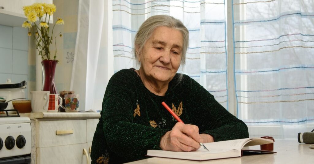 Nyugdíjas hölgy a konyhájában füzetbe jegyzetel