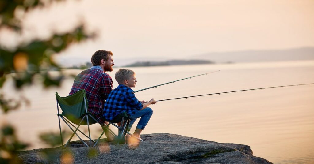 Apa és fia horgásznak egy tó partján naplementében