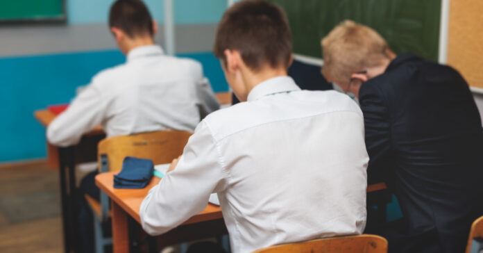 háttal ülő ünneplőben lévő diákok írnak valamit sulis padokban