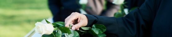 Egy kéz fehér rózsát helyez egy koporsóra temetési szertartáson