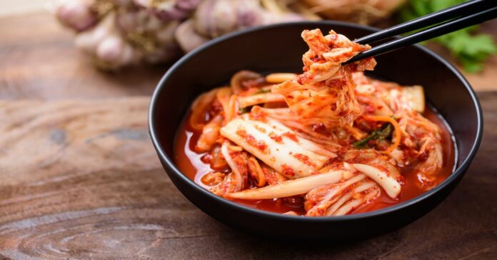 Fekete tálban kimchi, evőpálcikával felemelve háttérben fokhagyma