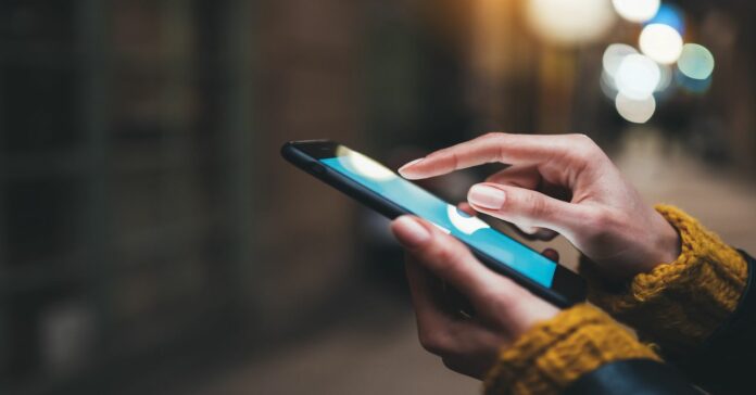 vodafone_aremeles_2024 Kéz okostelefont használ gyapjú kabátban, homályos háttérrel