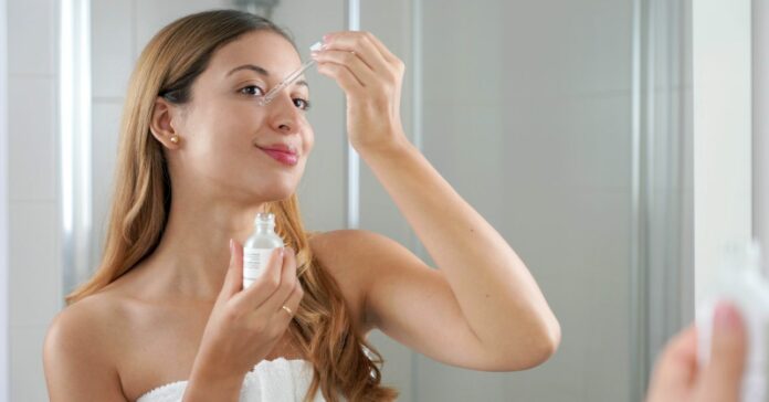 Bőrápolási rutin, fiatal nő C-vitamin szérumot csöpögtet az arcára a fürdőszobában