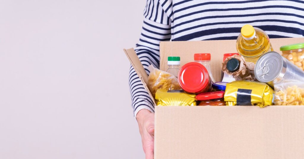 nő egy élelmiszer adománnyal teli dobozt tart a kezében