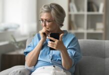 Alza közlemény: az applikáció a legjobb védelem az adathalászat és a csalók ellen Idősebb, visszafogottan öltözött hölgy ül a szürke kanapén aggódva fogva mobiletelefonját