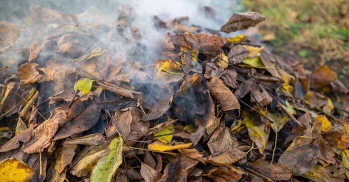 Egy halom összegereblyézett avar ég és füstöl, közeli kép