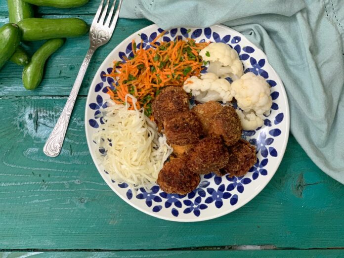 Sütőtökös falafel savanyúsággal és zöldségekkel ízlésesen tálalva, mutatós tányéron, zöldes színű asztalon
