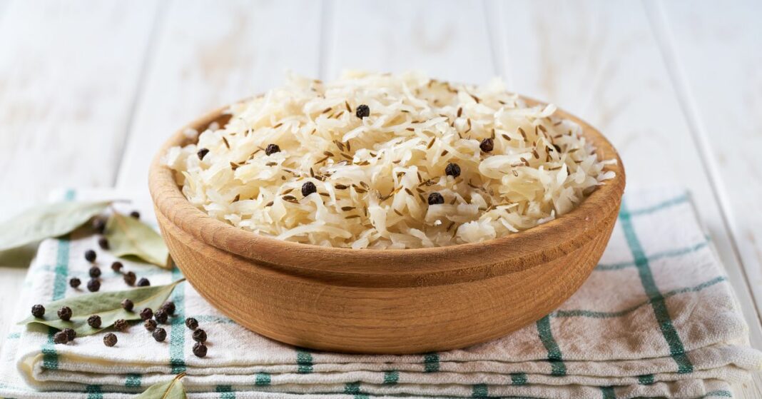 fermented white cabbage in a wooden bowl on a white kitchen table. Selective focus.
