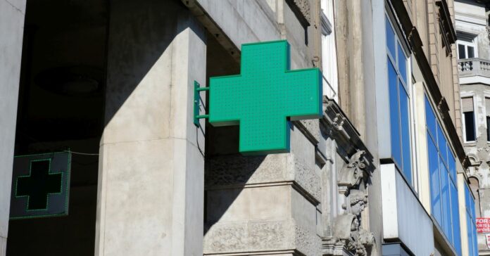 Zöld kereszt alakú tábla az épület homlokzatán, ami a gyógyszertárat jelenti, Budapest belvárosában,
