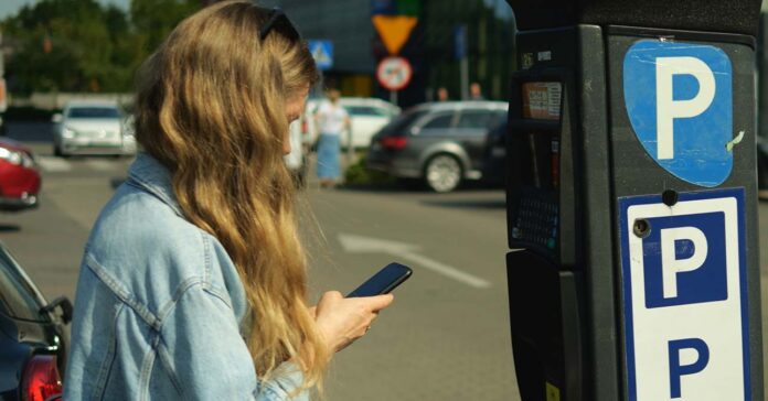 Mobilparkolás: fiatal nő éppen parkoló sms üzenetet küld a telefonjáról