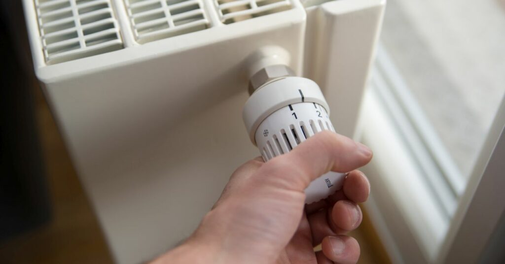 fűtőtest közelről, egy kéz 3-as fokozatra csavarja mennyi áramot fogyaszt az elektromos kazán