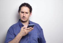 fiatal fehér férfi kék ingben gyanúsan néz a telefonjára