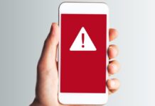 Fehér okostelefont tart a a kezében valaki, a mobilon figyelmeztető jelzés