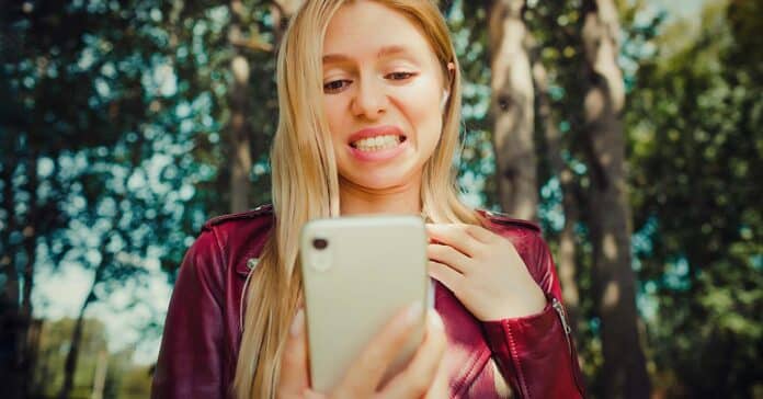 Fiatal nő, egy csalódott Apple felhasználó nézi a telefonját, érzelmei tükröződnek az arcán