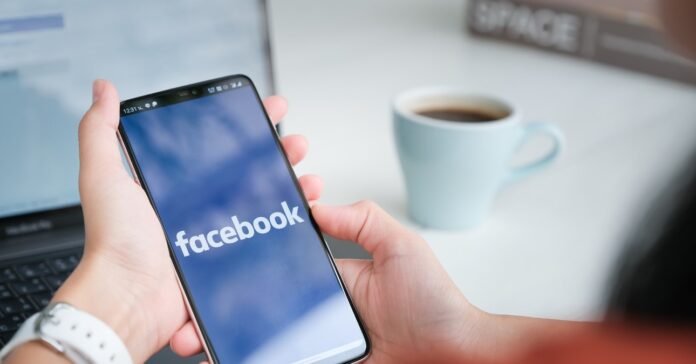 női kéz tart egy okostelefont, háttérben kávé és laptop