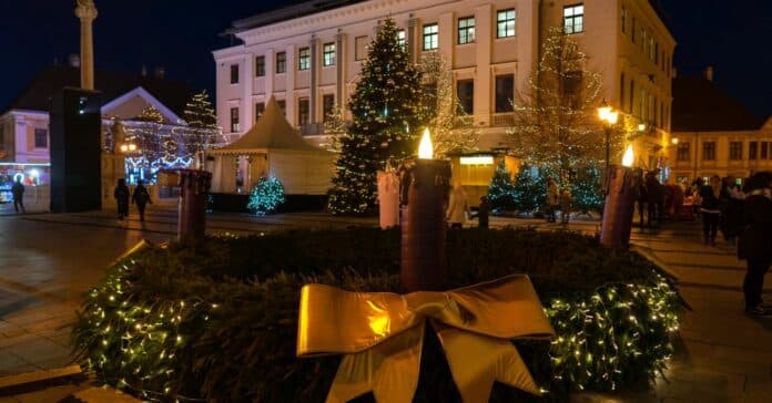 adventi vásár Győrben este emberekkel, nagy koszorúval a középpontban