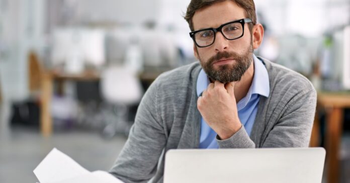 szemüveges férfi irodai asztalnál ül kezében papír