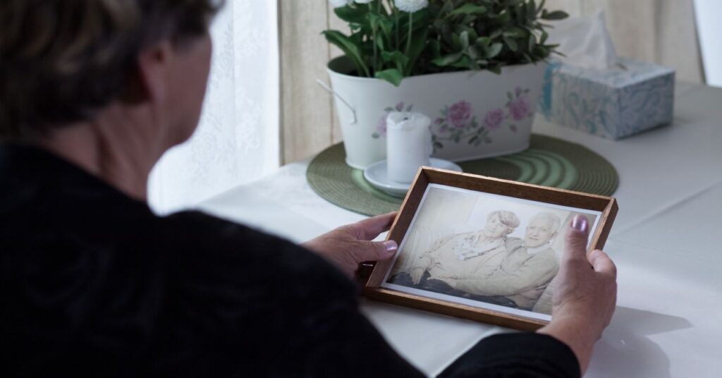 gyászoló, feketébe öltözött idős nő elhunyt férje fényképet nézi