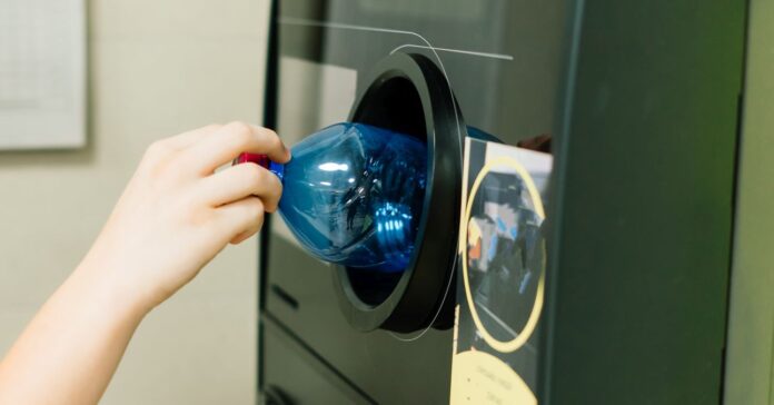 Egy automatába visszaváltható műanyag flakont dob be egy vásárló, közeli