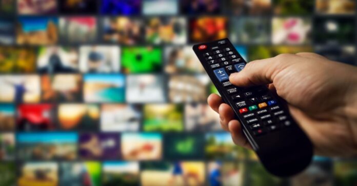 Egy távirányítót tart egy kéz a televízió felé