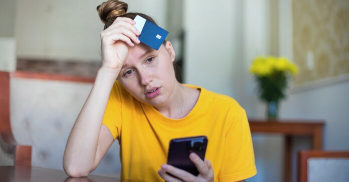 vegrehajtoi-letiltas-munkaberbol-2024 aggódó és értetlen nő telefonnal és bankkártyával a kezében