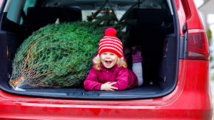 vidám kisgyerek karácsonyfával a kocsi csomagtartójában