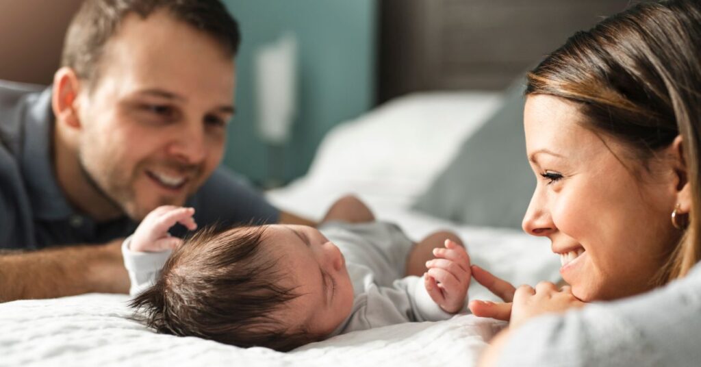 fiatal, boldog pár mosolyogva nézi a kisbabájukat