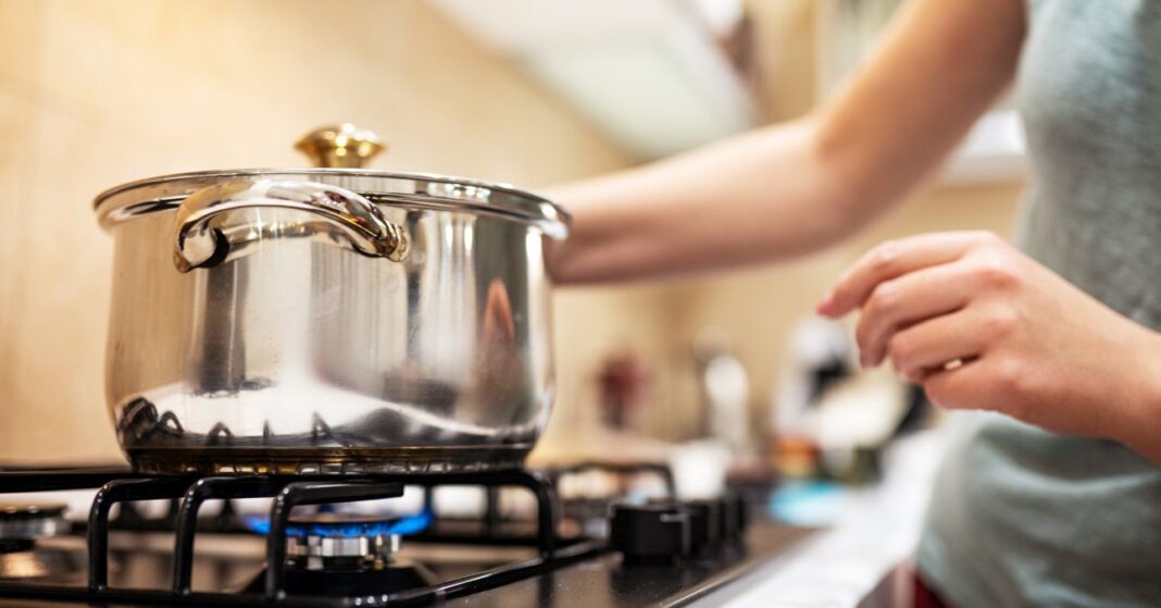 fiatal nő főz, a gáztűzhelyen egy edény fedővel lefedve, alatta ég a gáz