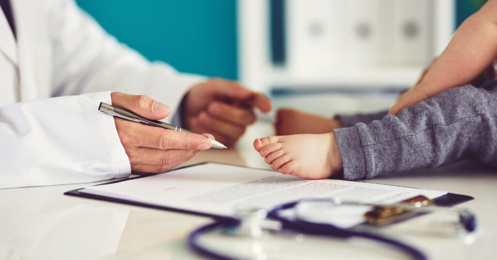 gyerekorvos asztalán kisgyerek ül, sztetoszkóppal és papírokkal