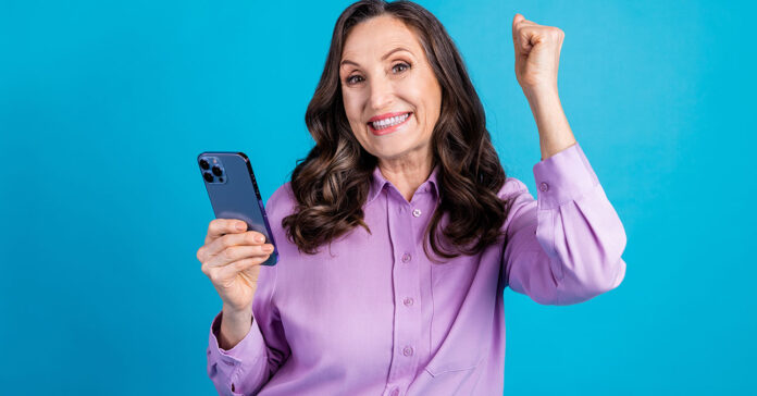 retro-kviz-lead Csinos nyugdíjas hölgy telefonnal a kézben örül, hogy megoldotta a retró kvízt