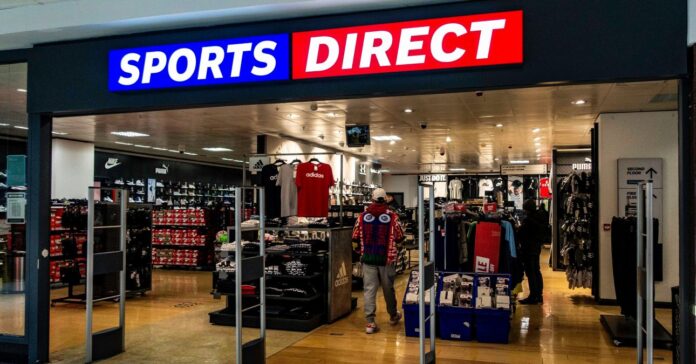 Az egyik SportsDirect üzlet bejárata cégtáblával, lopásérzékelős kapukkal, a háttérben sportcuccok