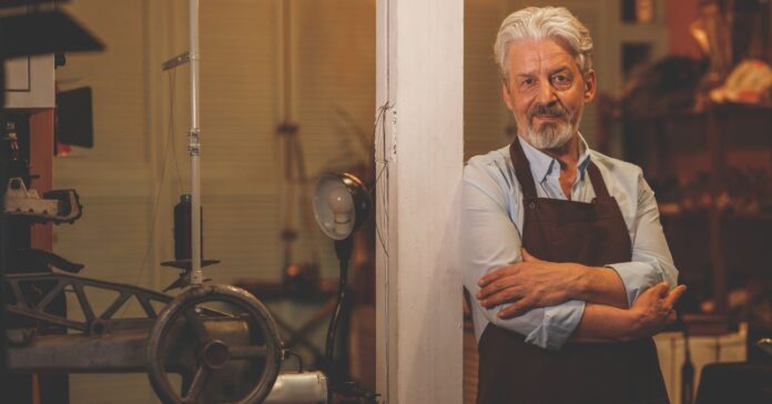 idősebb férfi kötényben áll és támasztja az oszlopot