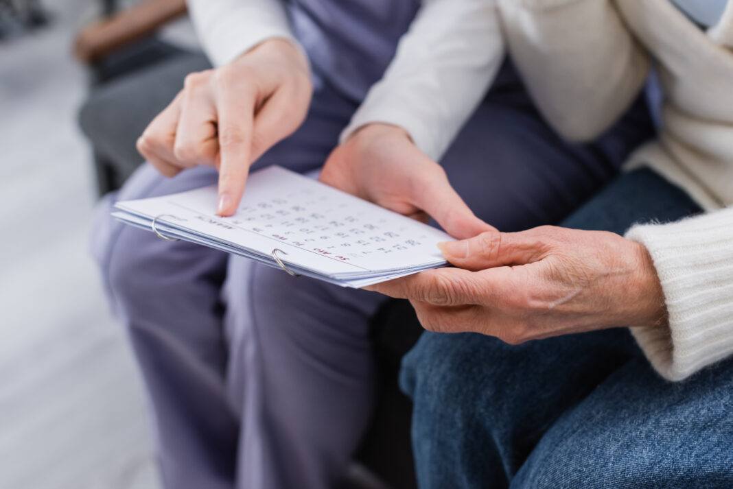 partial view of social worker pointing at calendar near aged wom
