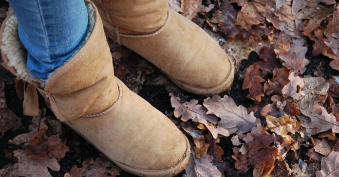 nő farmerben, világosbarna uggban áll az őszi avarban, közeli kép