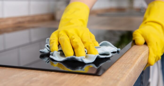 Young woman hands cleaning a modern black induction hob by a rag, housework indukciós főzőlap tisztítása mikroszálas kendővel