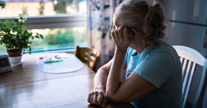 szomorú, magányos idős hölgy ül az asztalnál gondolataiba merülve