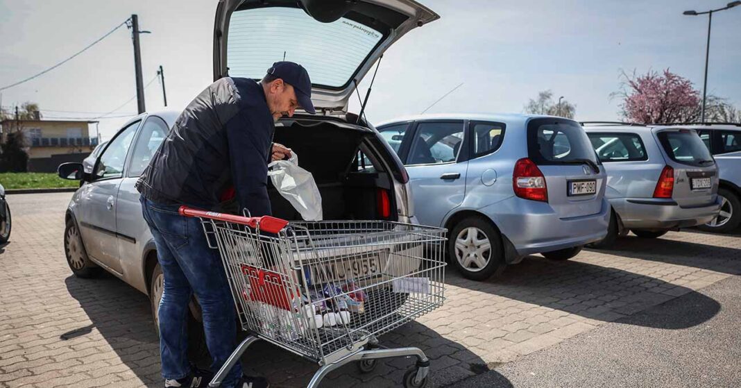 Egy férfi a bevásárlókosárból pakol az autó csomagtatójába