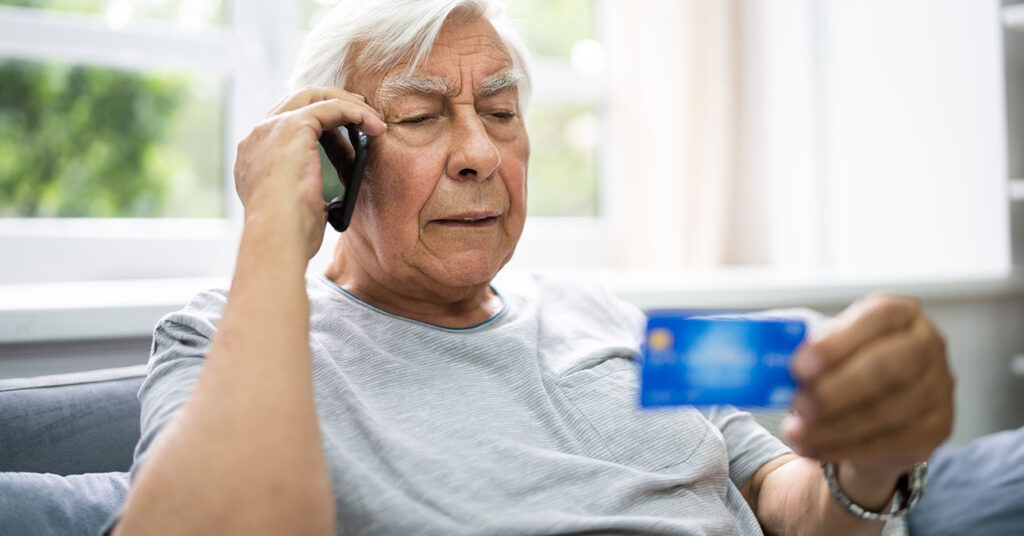 Csalók az online piactereken: idős ember telefonon diktálja be a bankkártyája titkos kódját
