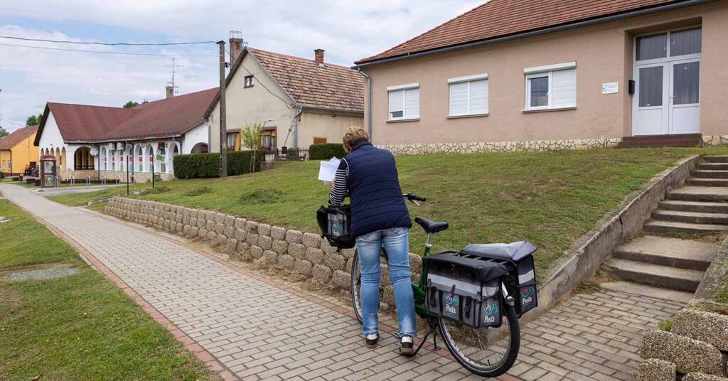 Egy postás áll egy vidéki ház előtt és kézbesíti a levelet