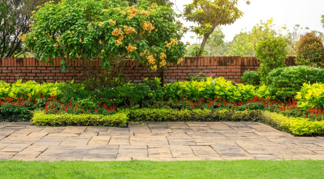 Backyard English cottage garden on brown pavement and green lawn