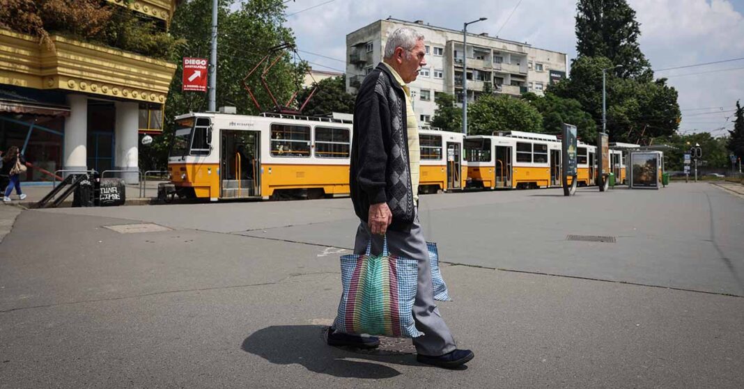nyugdíjas férfi szatyrokkal sétál egy villamos megálló mellett