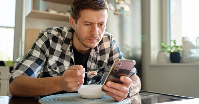 Reggelizés közben mobilozik a fiatal férfi az asztalánál - az ingercsökkentő környezet kialakításával sokat nyerne