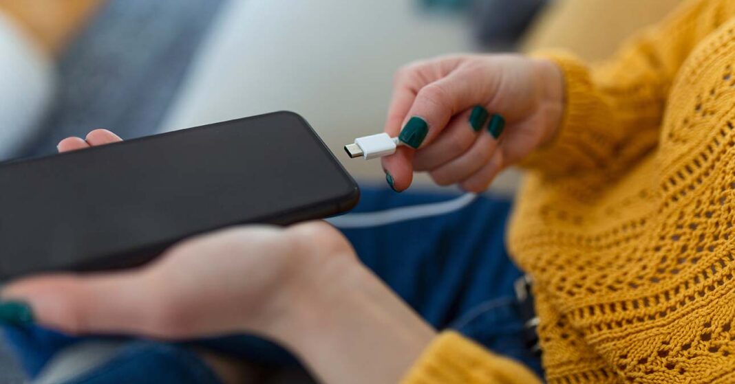 mobiltelefon-tolto-power-bank Hogyan lehet telefont tölteni töltő nélkül? A képen például egy külső akkumulátort vagy power banket csatlakoztat egy sárga pulóveres nő a telefonjára.
