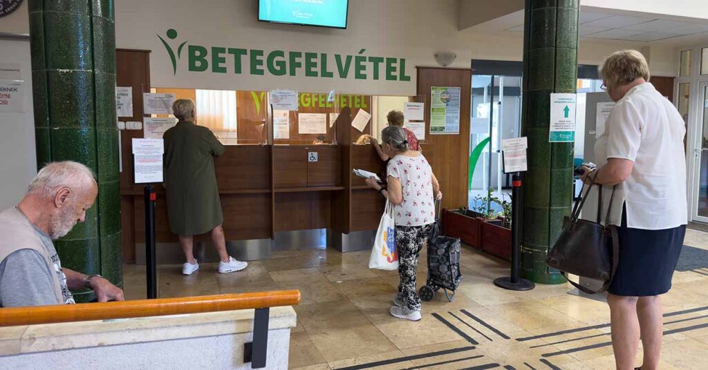 egészségügyi intézményben betegfelvétel, pult előtt sorban álló emberek