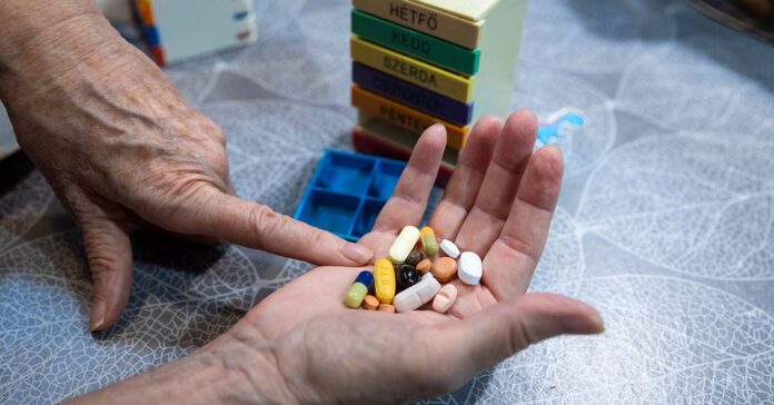 gyógyszereket tart a markában egy idős nő, előtte gyógyszeradagoló